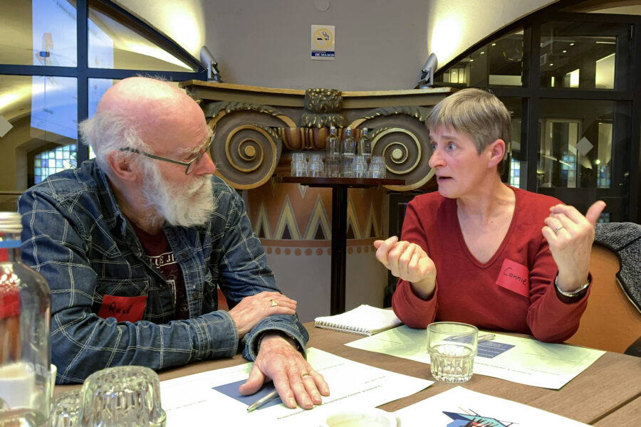 Een man en een vrouw zitten naast elkaar aan ta fel en zijn met elkaar in gesprek.